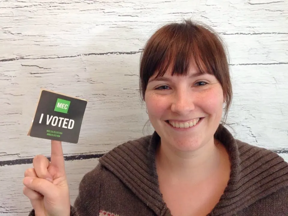 A woman holds up a sticker that says MEC I voted