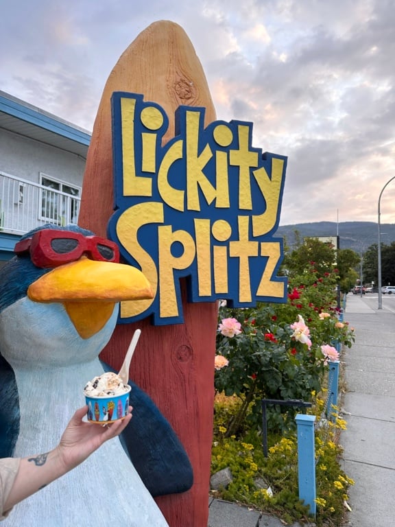 A hand holds a cup of ice cream in front of a penguin statue at Lickity Splitz ice cream in Penticton