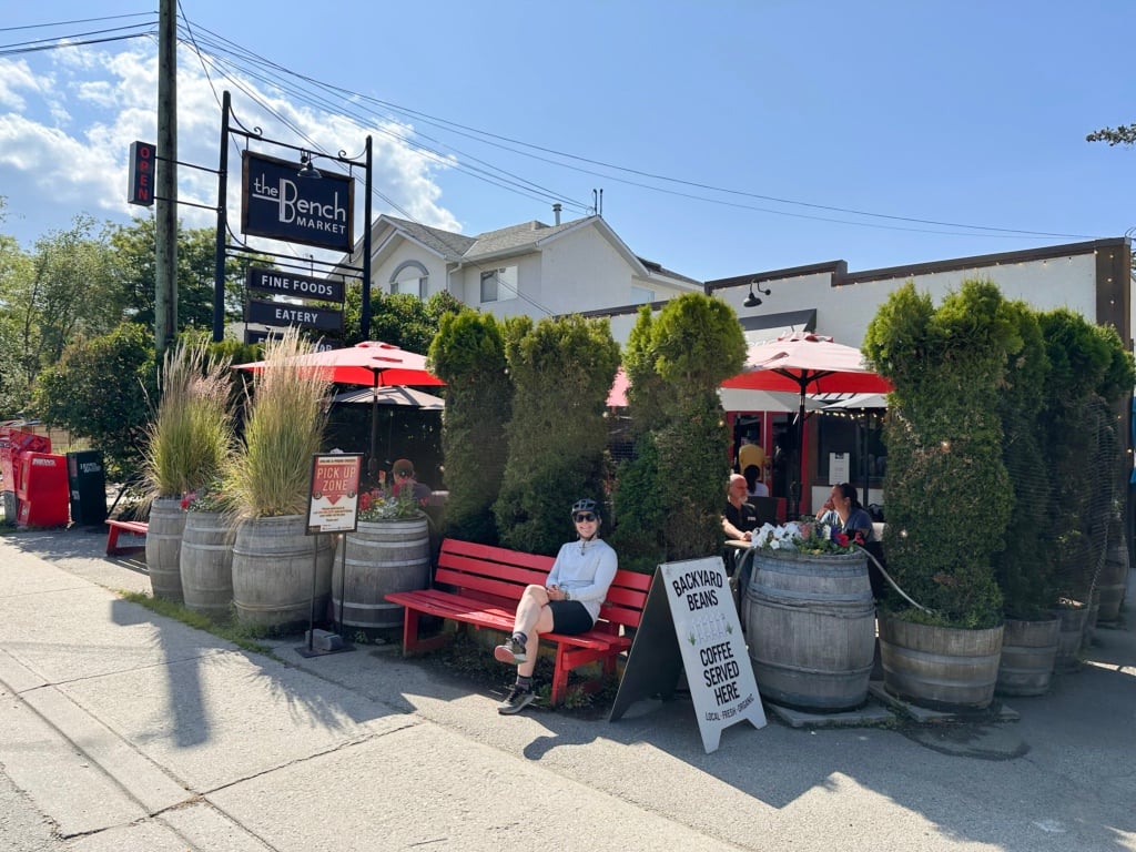 A woman wearing a bike helmet sits on a bench outside The Bench Market in Penticton