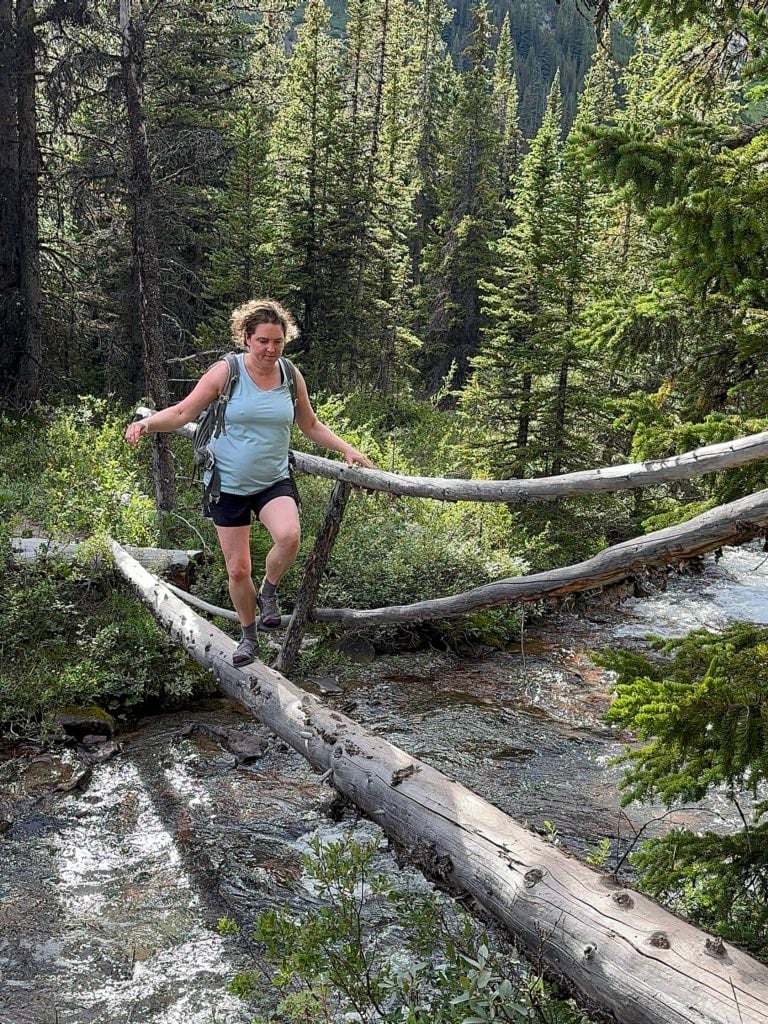 A hiker crosses a log bridge on the Merlin Lake Trail