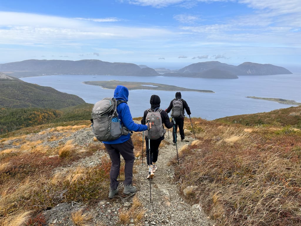 HIkers descending the Cape Blow Me Down Trial with Bay of Islands in the background.