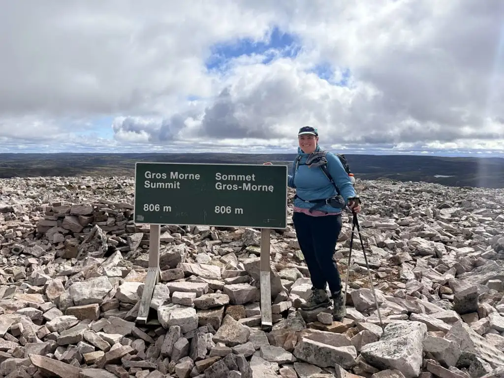 A woman poses with the summit sign at the top of Gros Morne Mountain