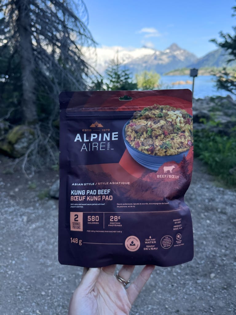 A hiker holds a package of Alpine Aire Kung Pao Beef close to the camera