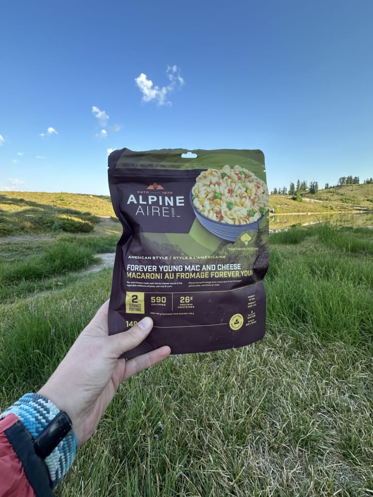 A hiker holds a package of Alpine Aire Forever Young Mac and Cheese