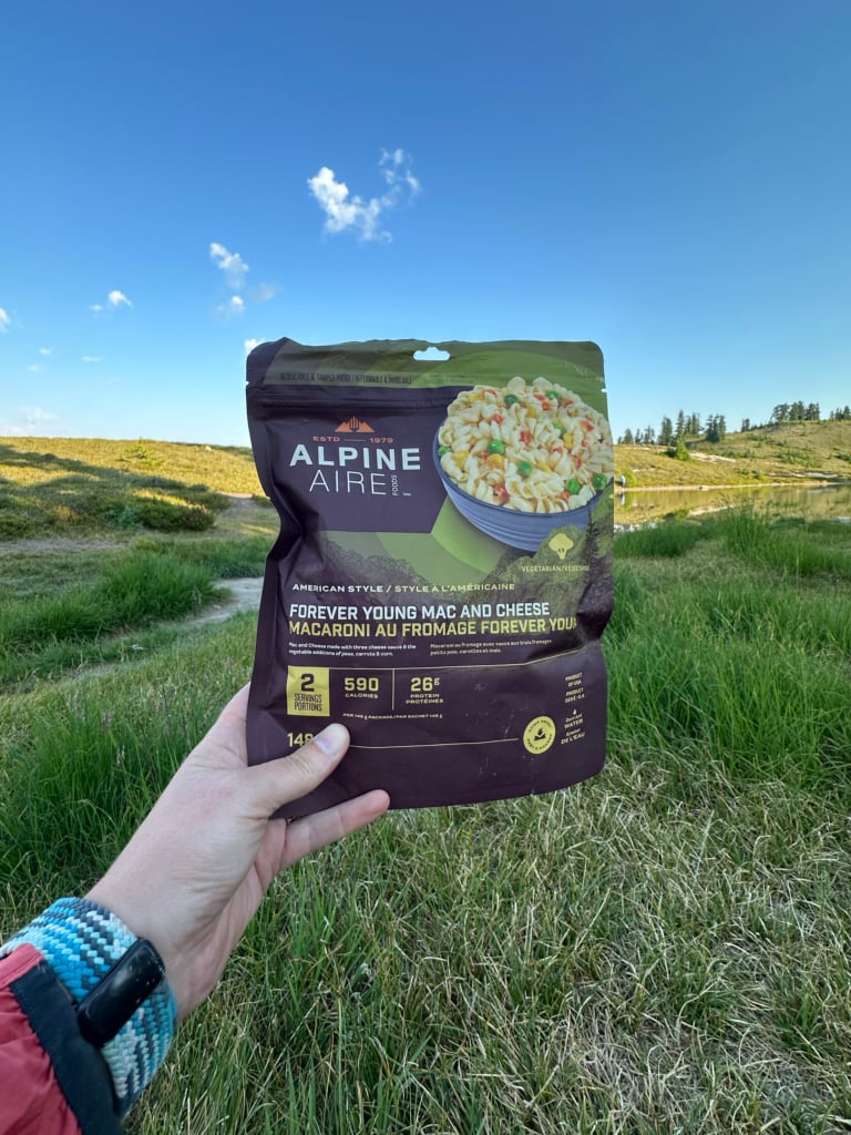A hiker holds a package of Alpine Aire Forever Young Mac and Cheese