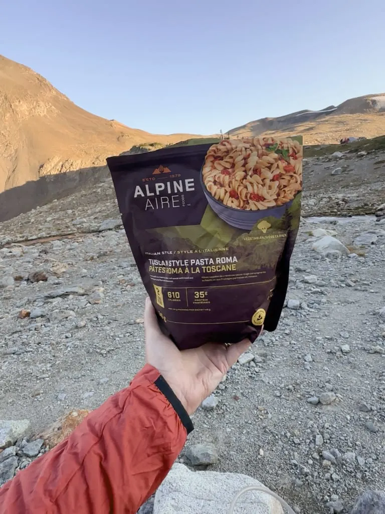 A hiker holds a package of Alpine Aire Tuscan Style Pasta Roma