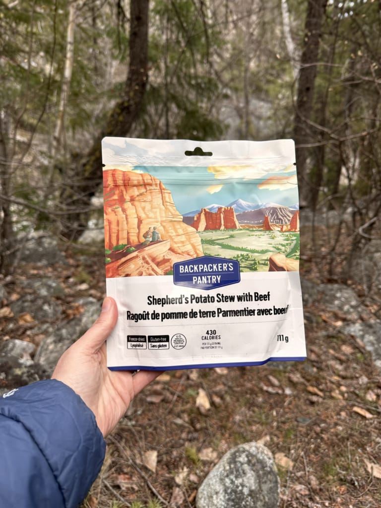 A backpacker holds a package of Backpacker's Pantry Shepherd's Potato Stew with Beef
