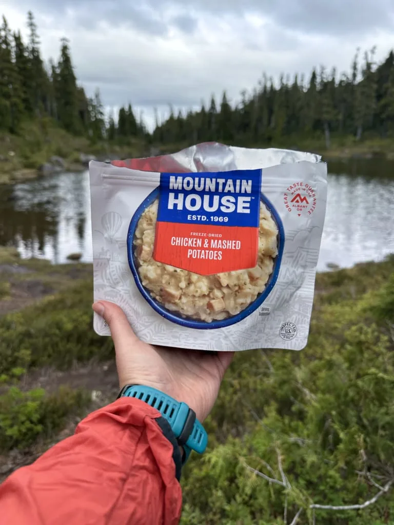 A hiker holds a package of Mountain House Mashed Potatoes with Chicken
