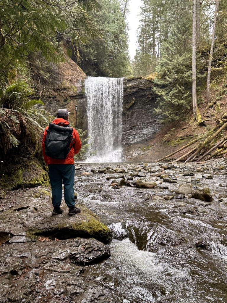 A man wearing an orange rain jacket stands in front of Ammonite Falls