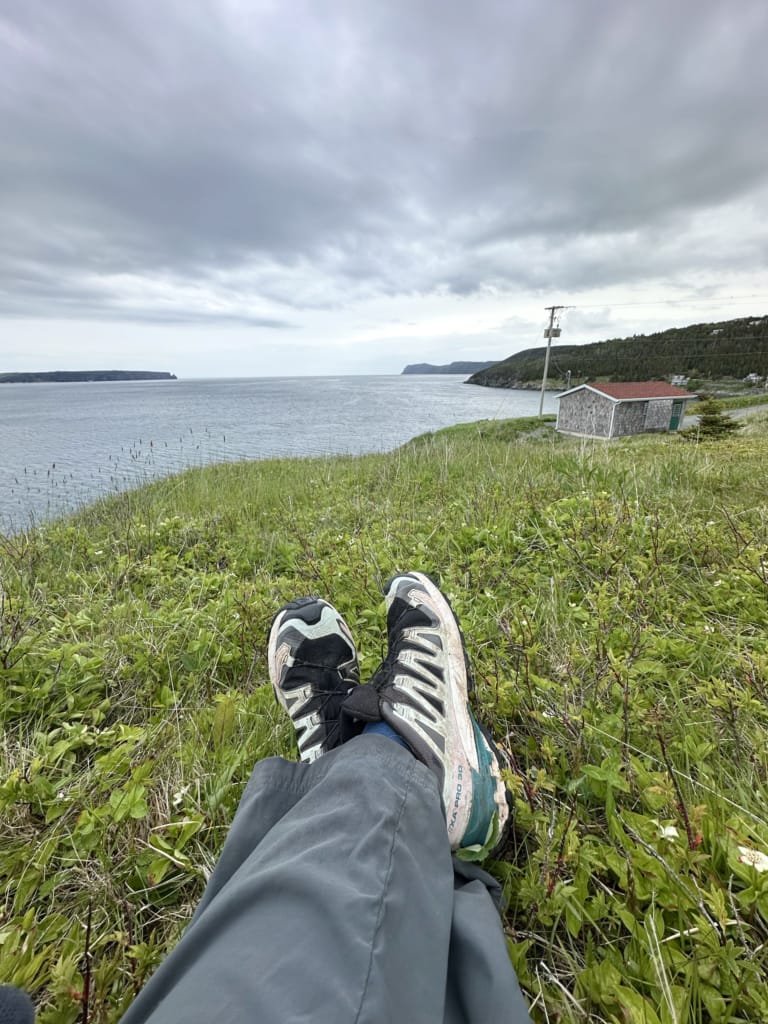 A hiker takes a photo of their legs and feet stretched out on a bluff on the East Coast Trail