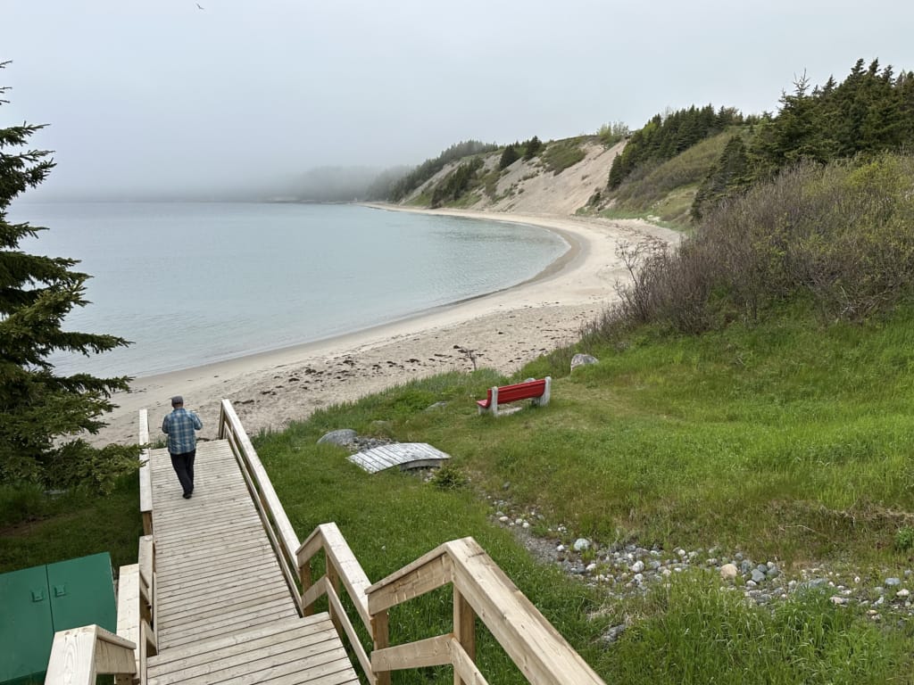 A man walks down a wooden staircase to a sandy beach on the Eastport Peninsula in Newfoundland