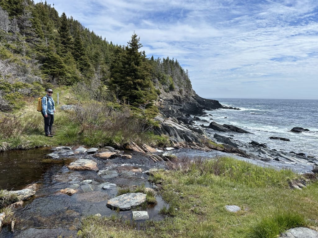 A hiker crossing Chance River on the Spurwink Island Path on the East Coast Trail