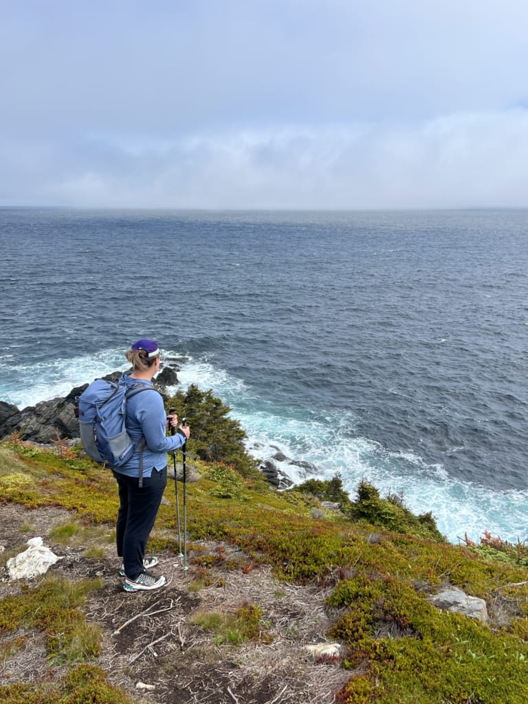 A hiker stands on a cliff looking at the ocean on the East Coast Trail