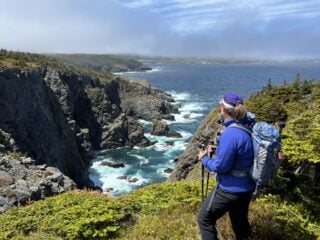 A female hiker looks at an ocean view from a clifftop trail on the Stiles Cove Path on the East Coast Trail in Newfoundland