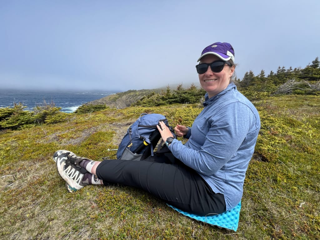 A hiker sits on a foam sit pad on the East Coast Trail